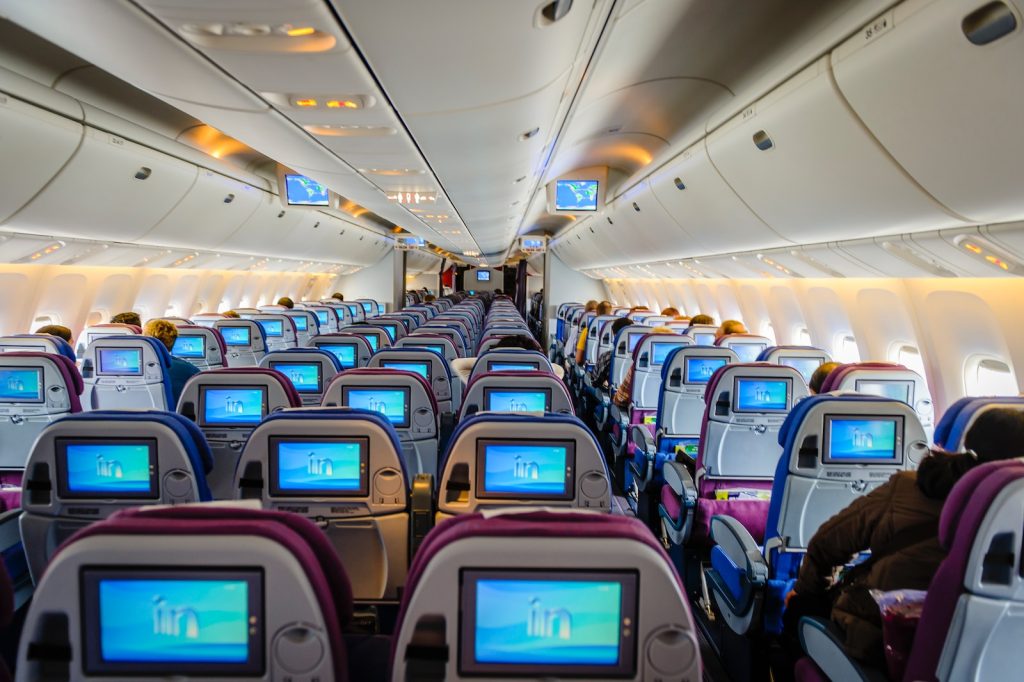 Interior of aeroplane cabin with passengers seated and in-flight entertainment screens visible