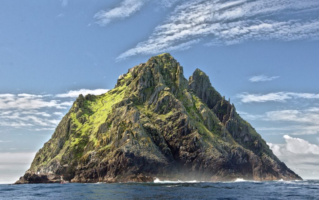 Majestic rocky island with lush green slopes rising from the blue sea under a bright sky, Skellig Michael Ireland