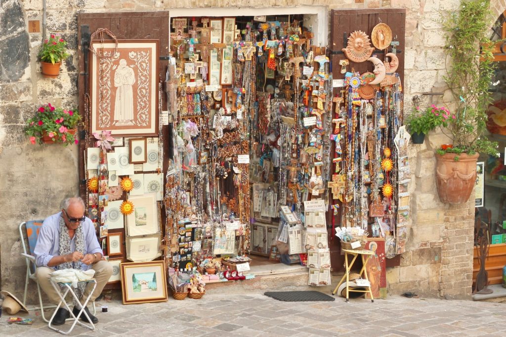 Colourful market stall with hanging trinkets, artwork and decor, old man sitting nearby in a quaint street setting