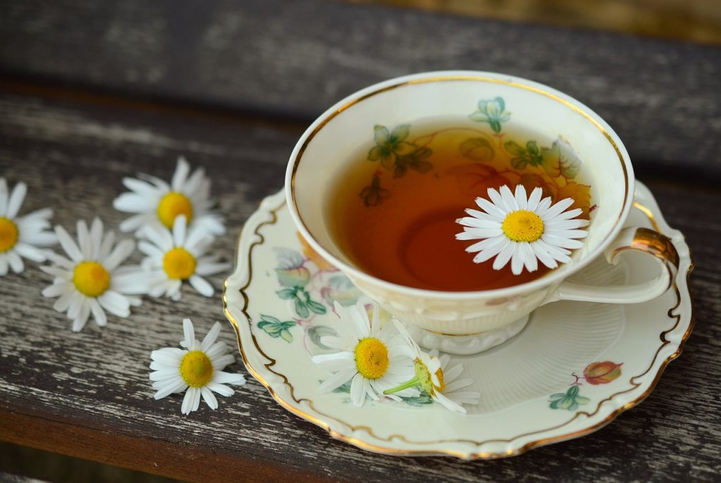Vintage teacup with chamomile flowers floating in herbal tea on a rustic wooden table for a calming atmosphere
